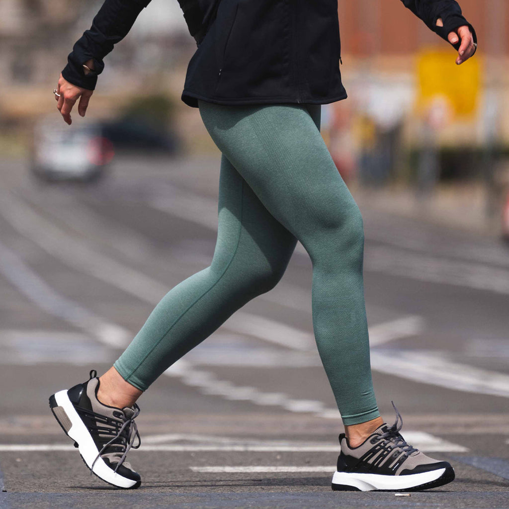 En person med grønne bukser har på seg sneakeren Advance Pro fra GaitLine i fargen fudge mens hun går på asfalt