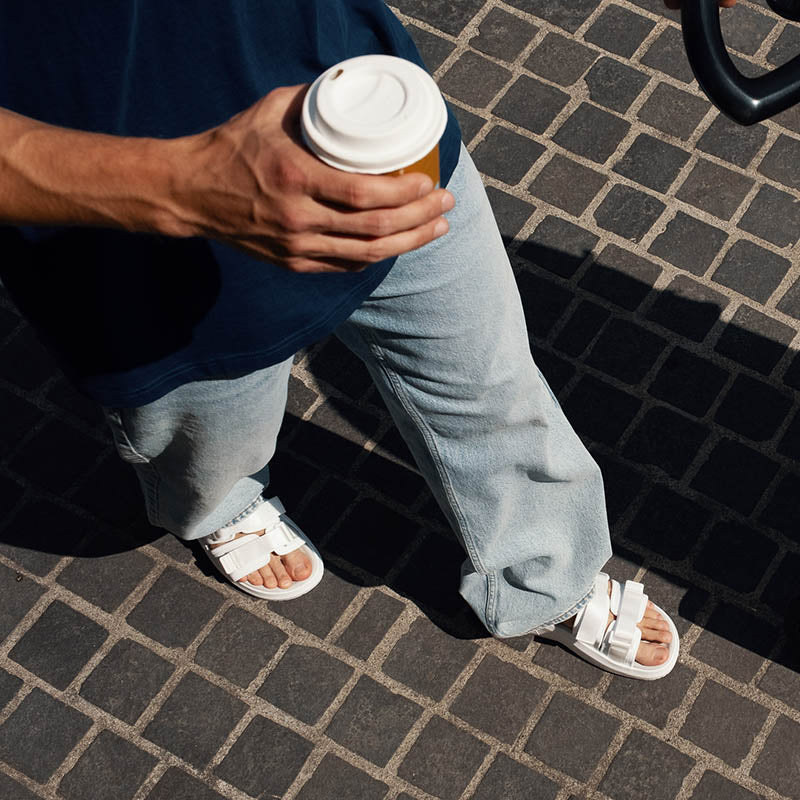 Mann med jeans som holder i kaffekopp har på seg Flow SP Sandal i hvit